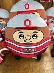 Plush toy resembling a cartoon character with a helmet and 'O' logo, labeled 'Brutus', on a wooden surface.