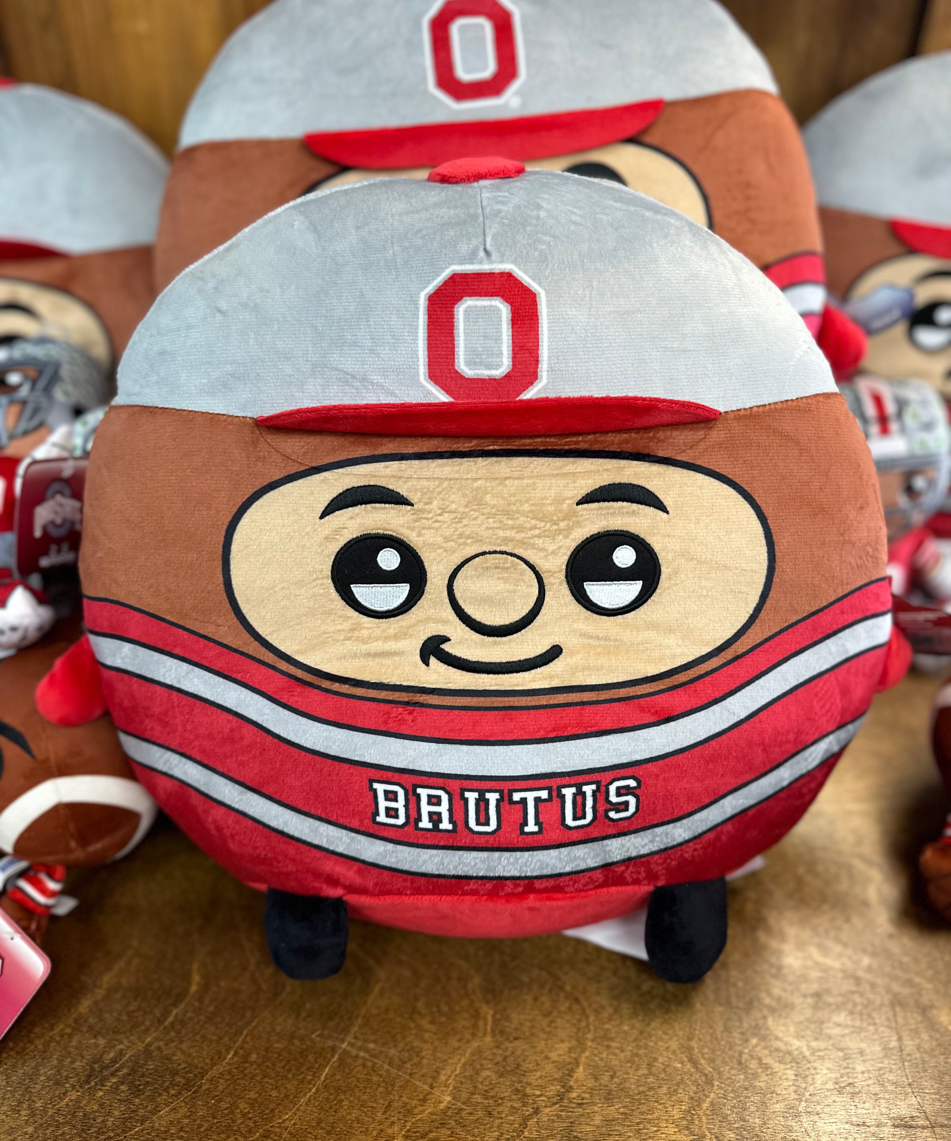 Plush toy resembling a cartoon character with a helmet and 'O' logo, labeled 'Brutus', on a wooden surface.