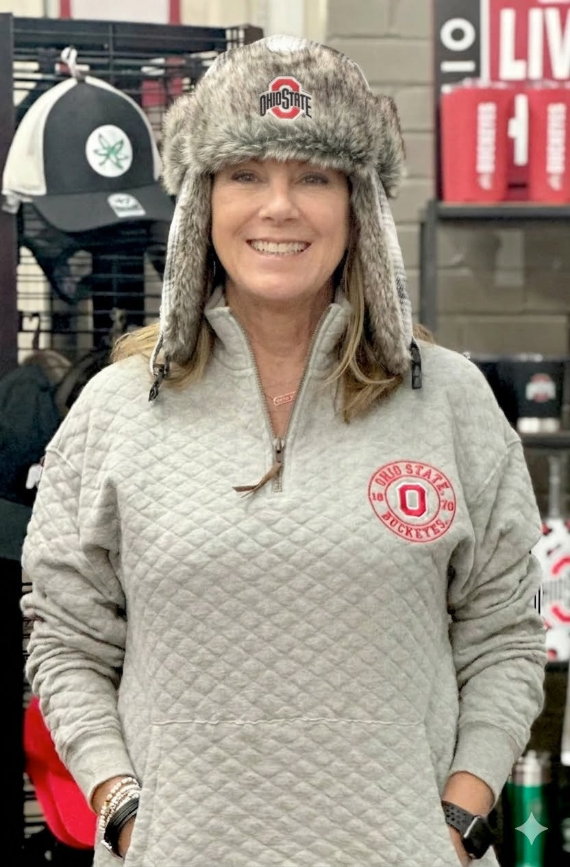 Person wearing a gray quilted jacket with a logo and a fur-trimmed hat in a store setting.