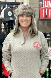 Person wearing a gray quilted jacket with a logo and a fur-trimmed hat in a store setting.