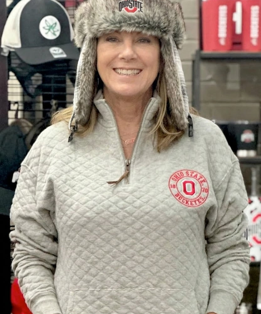 Person wearing a gray quilted jacket with a logo and a fur-trimmed hat in a store setting.