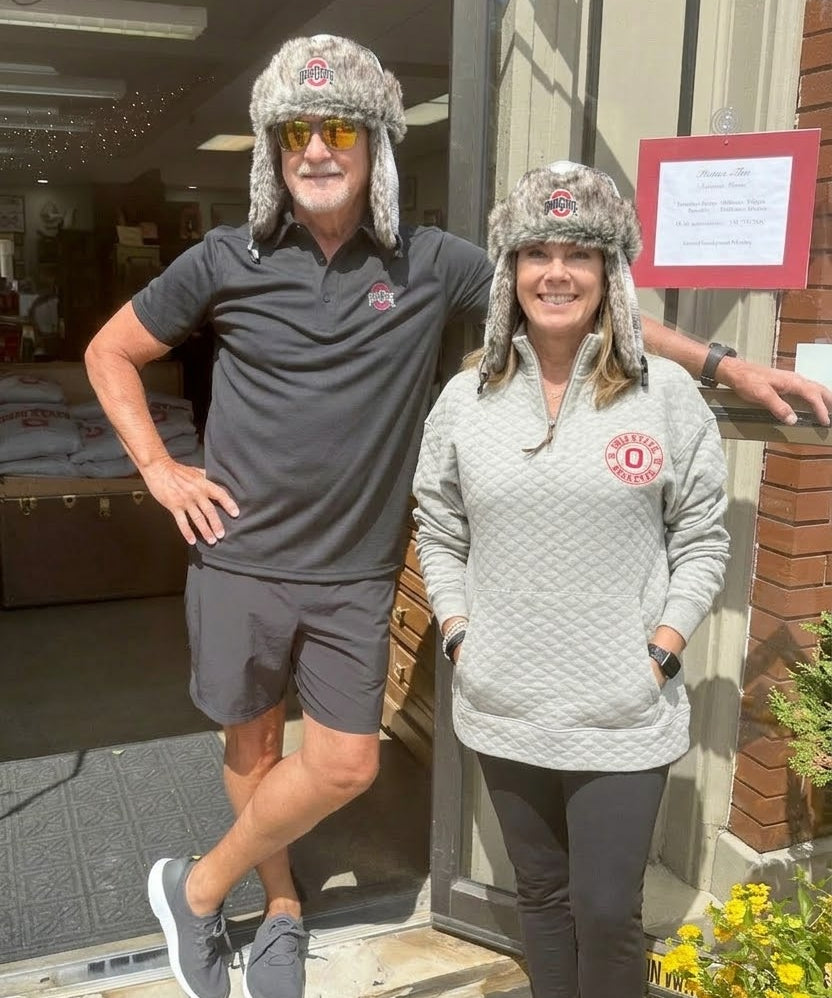 Two people wearing matching gray fur hats standing outside a building.