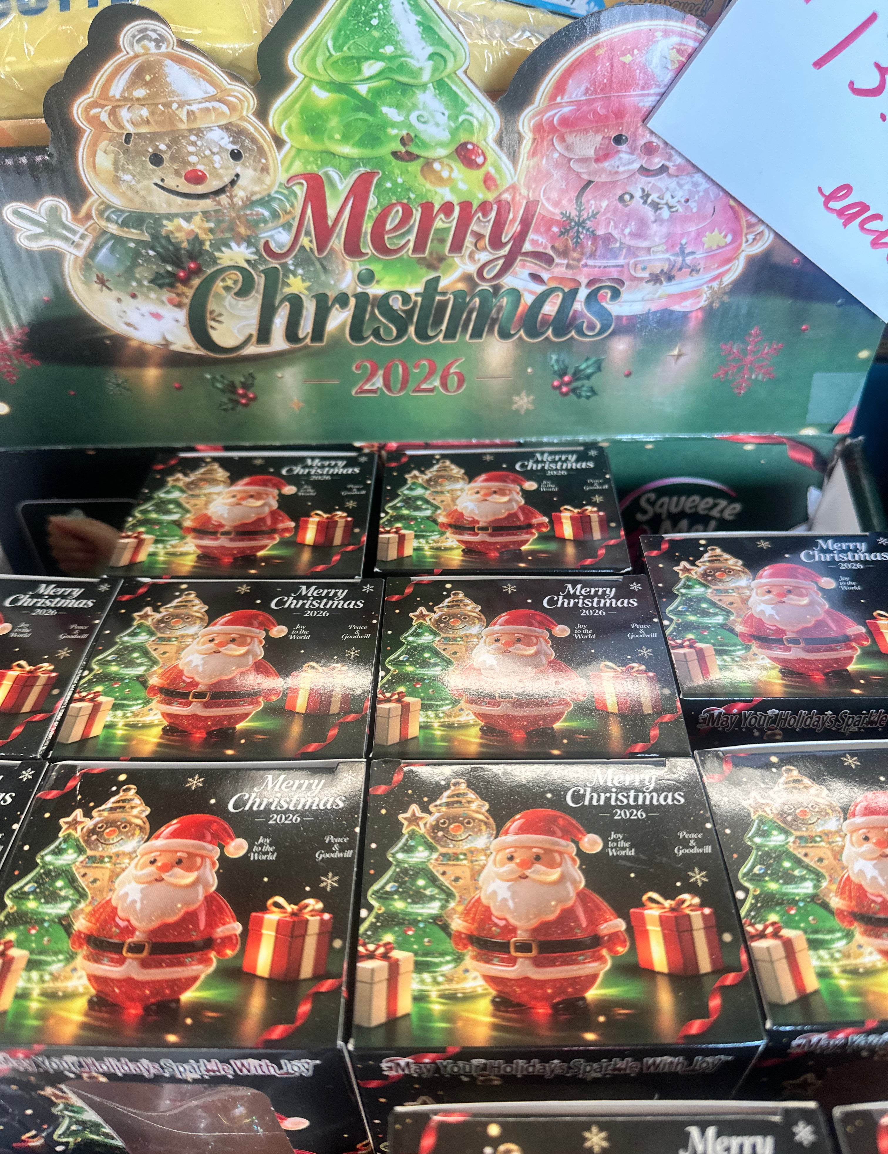 A retail display of Santa Claus Christmas ornament boxes with 'Merry Christmas 2026' holiday graphics on the packaging, photographed in a store setting.