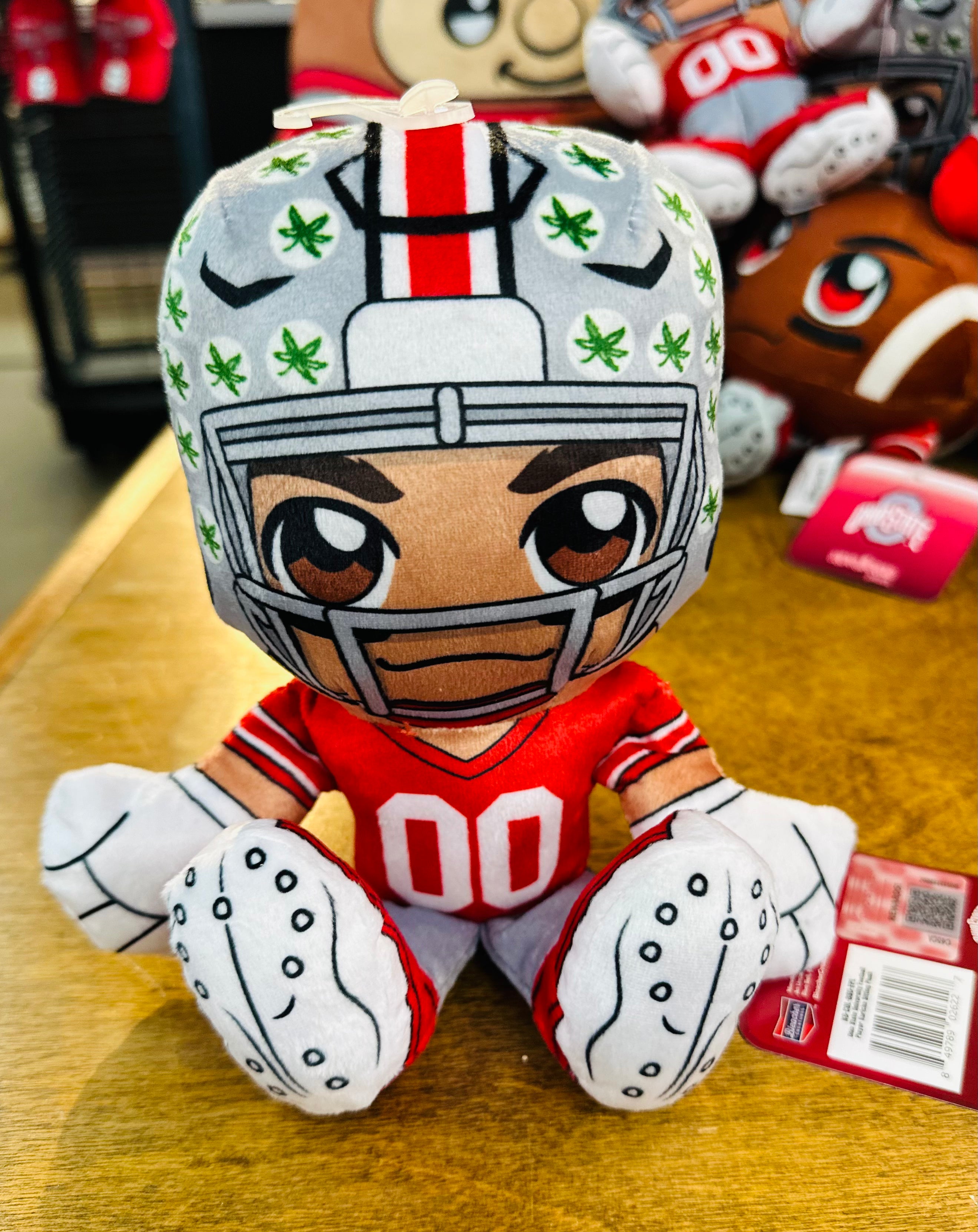 Plush toy of a football player in a helmet with green patterns on a wooden surface.