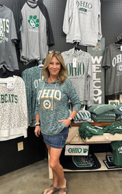 Woman wearing a green 'OHIO' sweatshirt in a store with various clothing items on display.