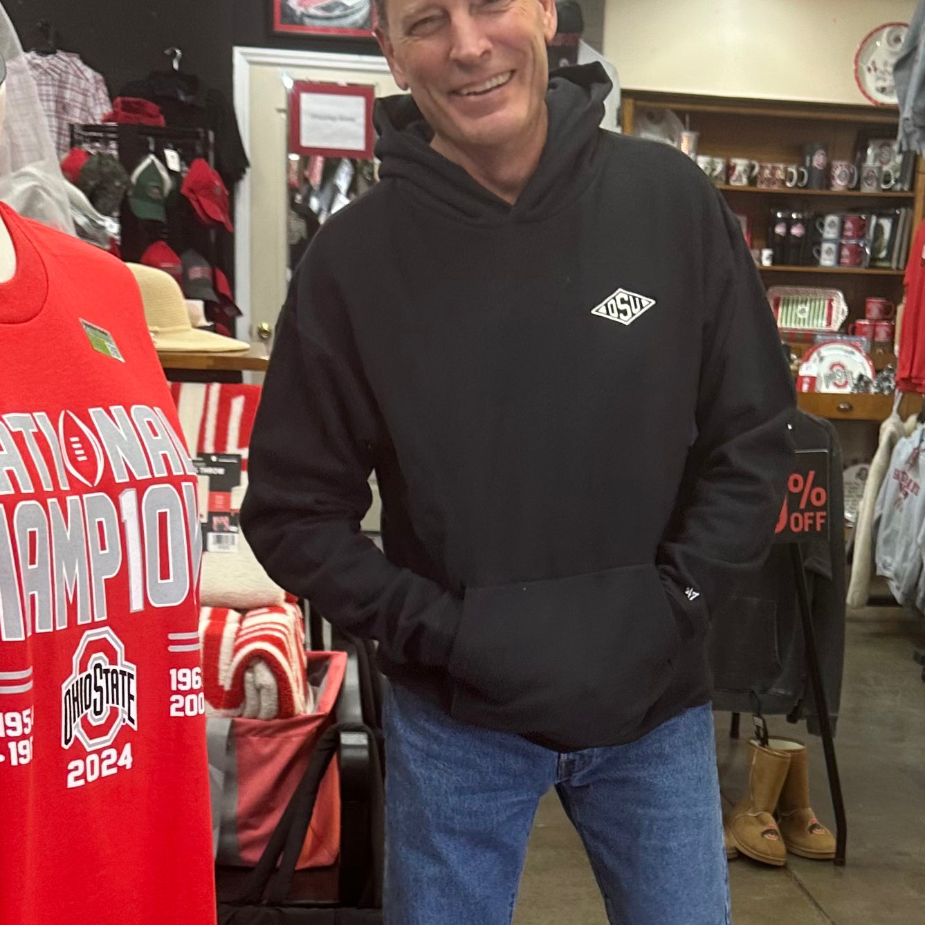 Man wearing a black hoodie with a logo in a store setting