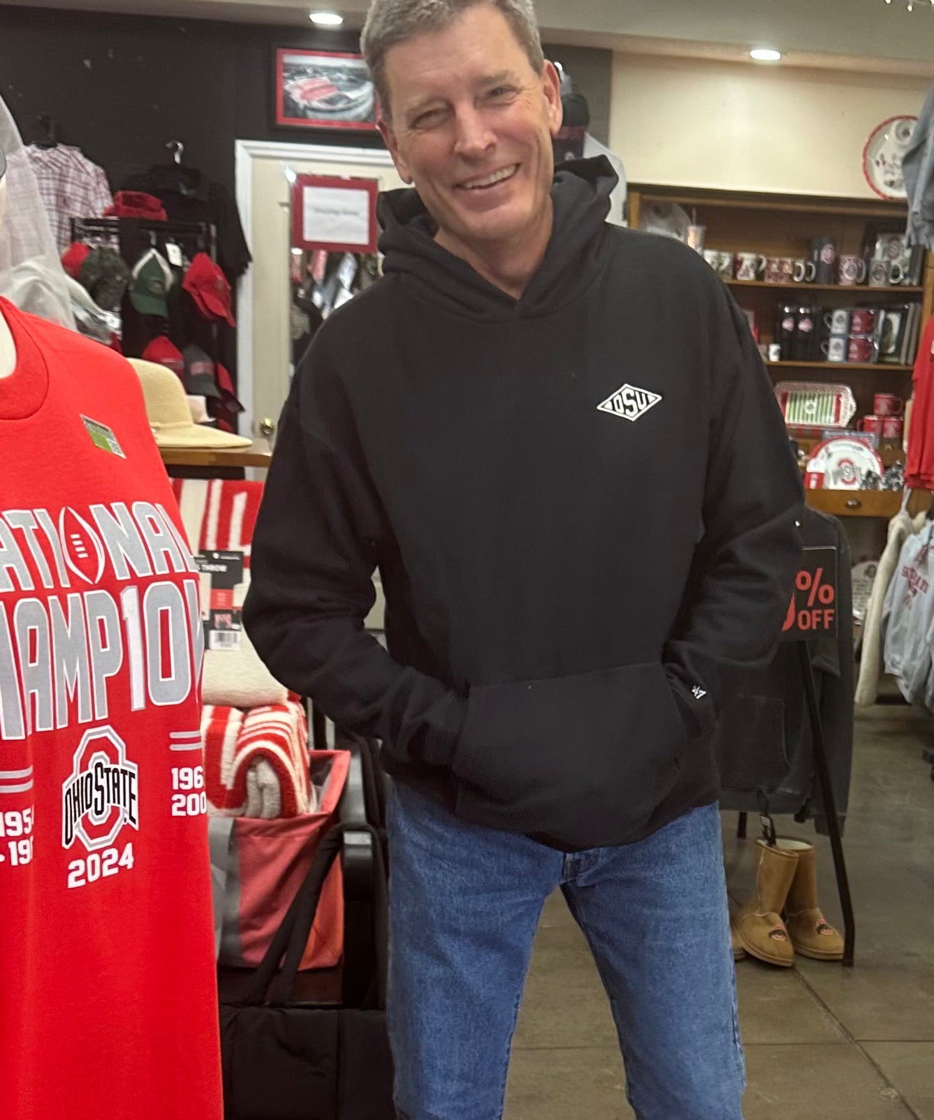 Man wearing a black hoodie with a logo in a store setting