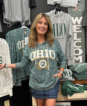Woman wearing a green 'OHIO' sweatshirt in a store setting with various clothing items around.