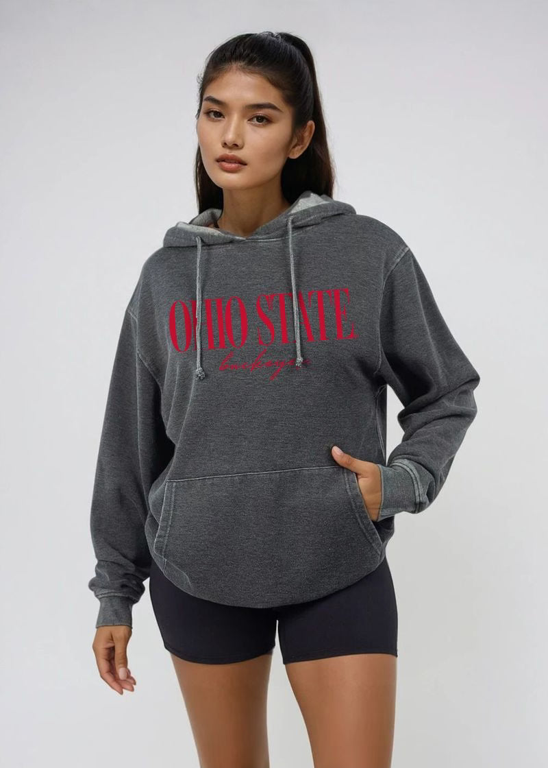 A woman modeling a dark gray heathered hoodie with 'OHIO STATE' printed in red across the chest, paired with black bike shorts, against a light gray studio background.