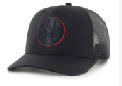 A black trucker-style baseball cap with a curved brim, black mesh back panels, and a circular embroidered logo on the front with a red outline.