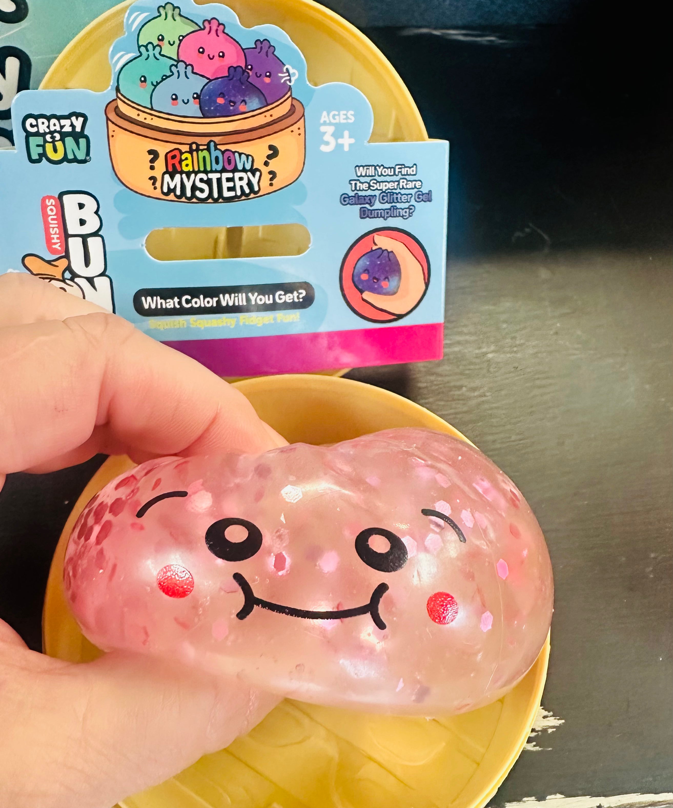 Pink squishy toy with a smiley face held in front of its packaging.