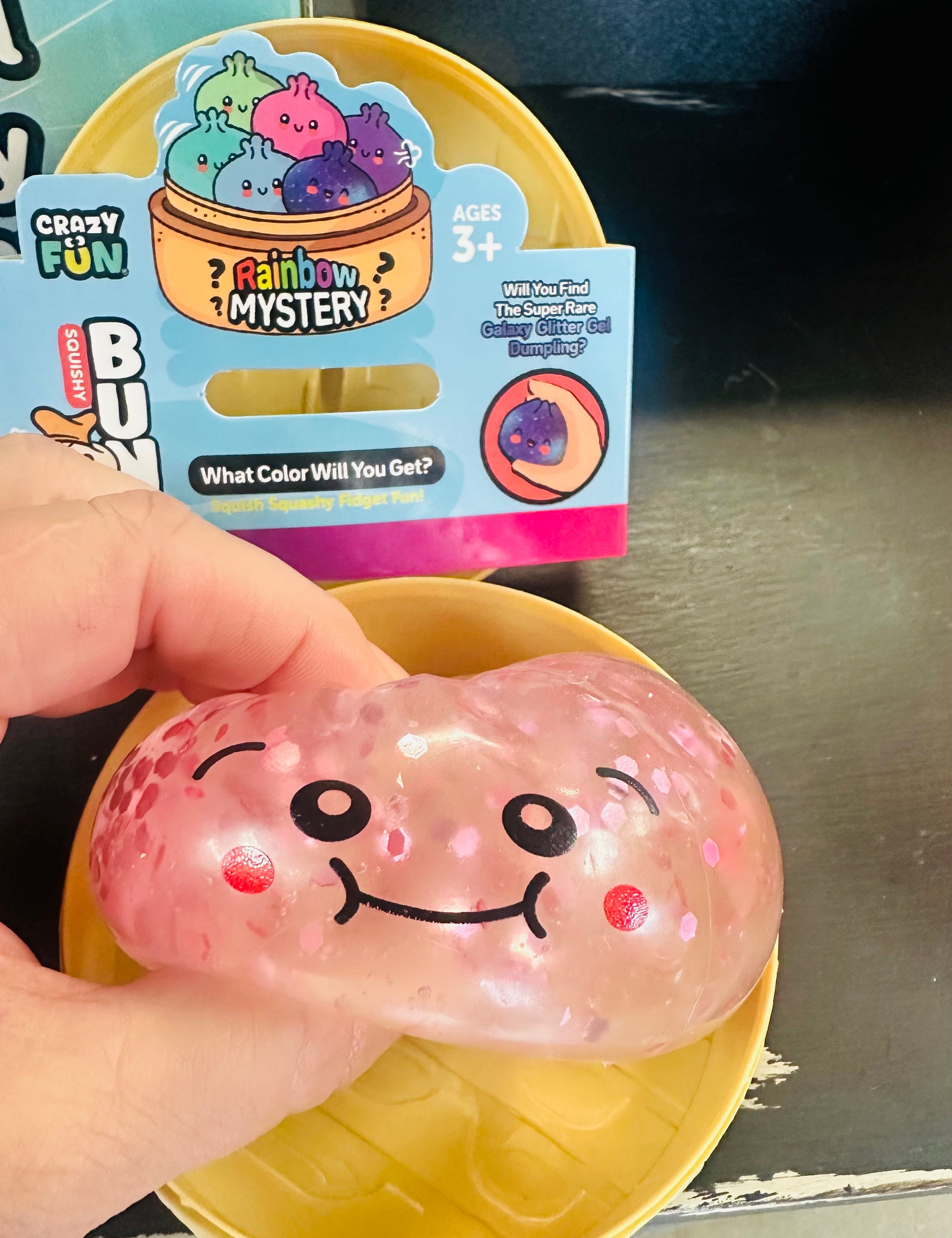 Pink squishy toy with a smiley face held in front of its packaging.