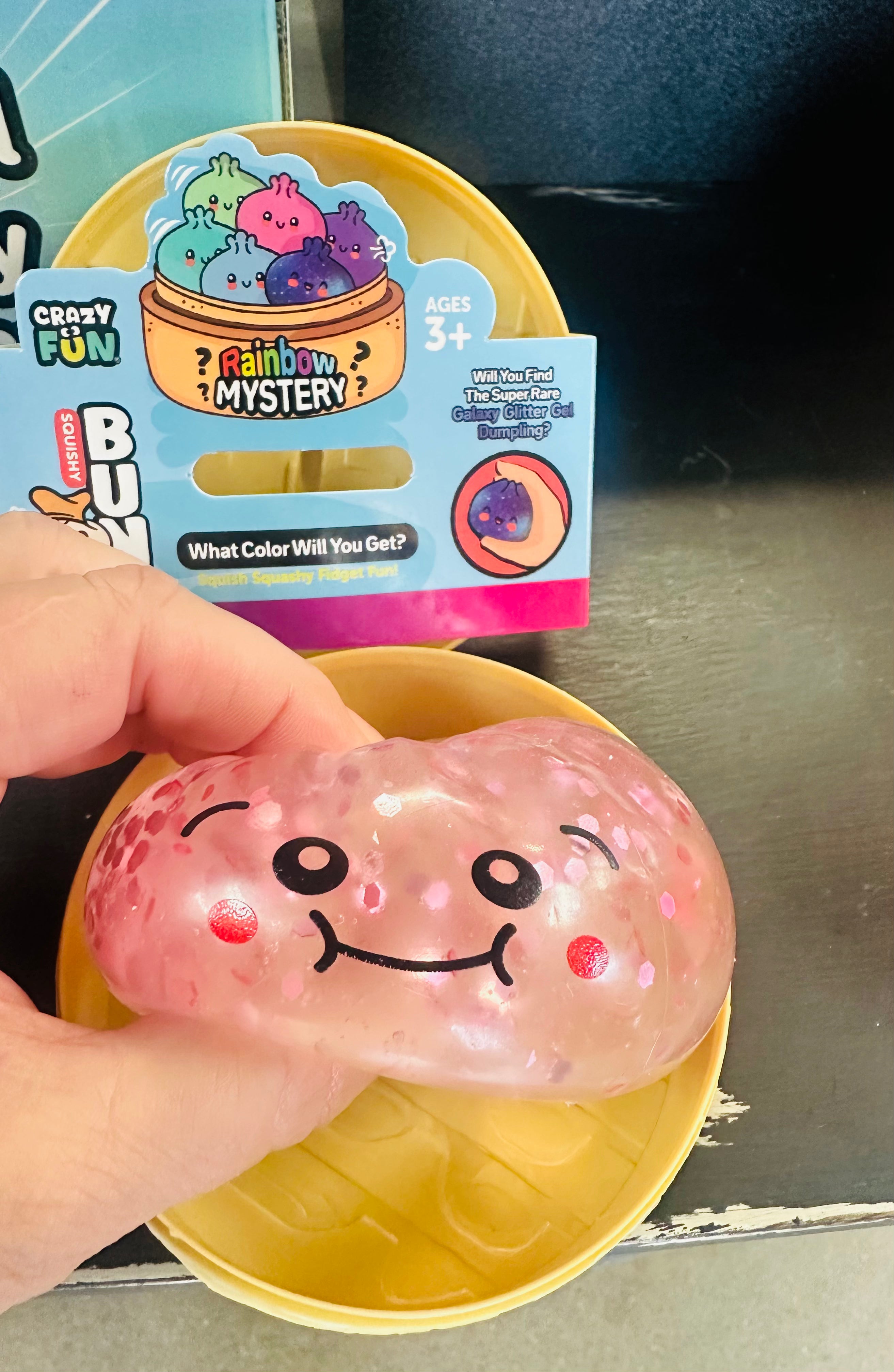 Pink squishy toy with a smiley face held in front of its packaging.