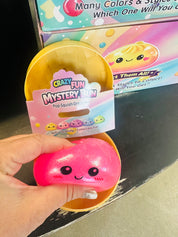 Pink squishy toy with a 'Crazy Fun Mystery Bin' packaging in front of a colorful box.