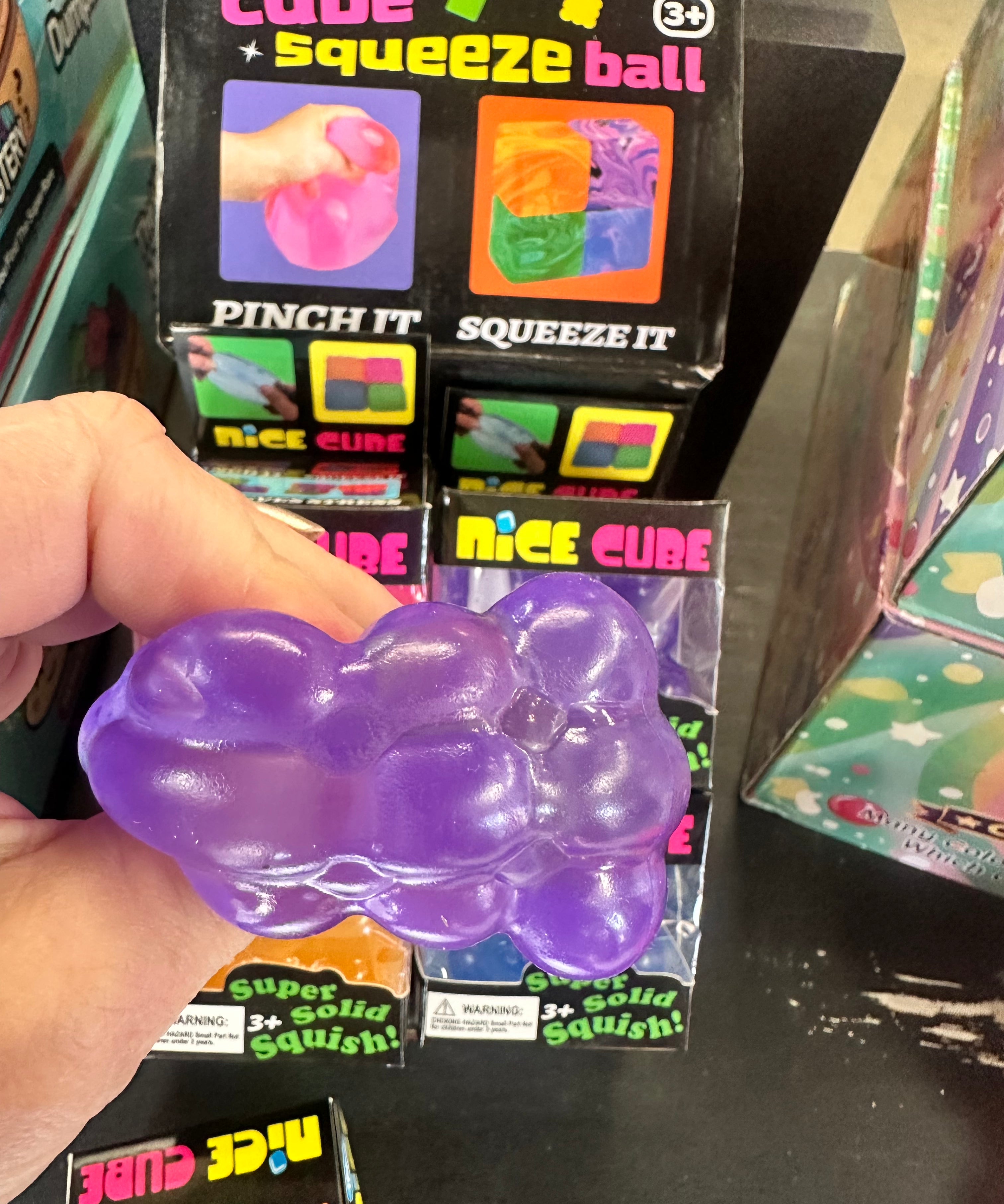 Purple cube squeeze ball held by a hand with packaging in the background