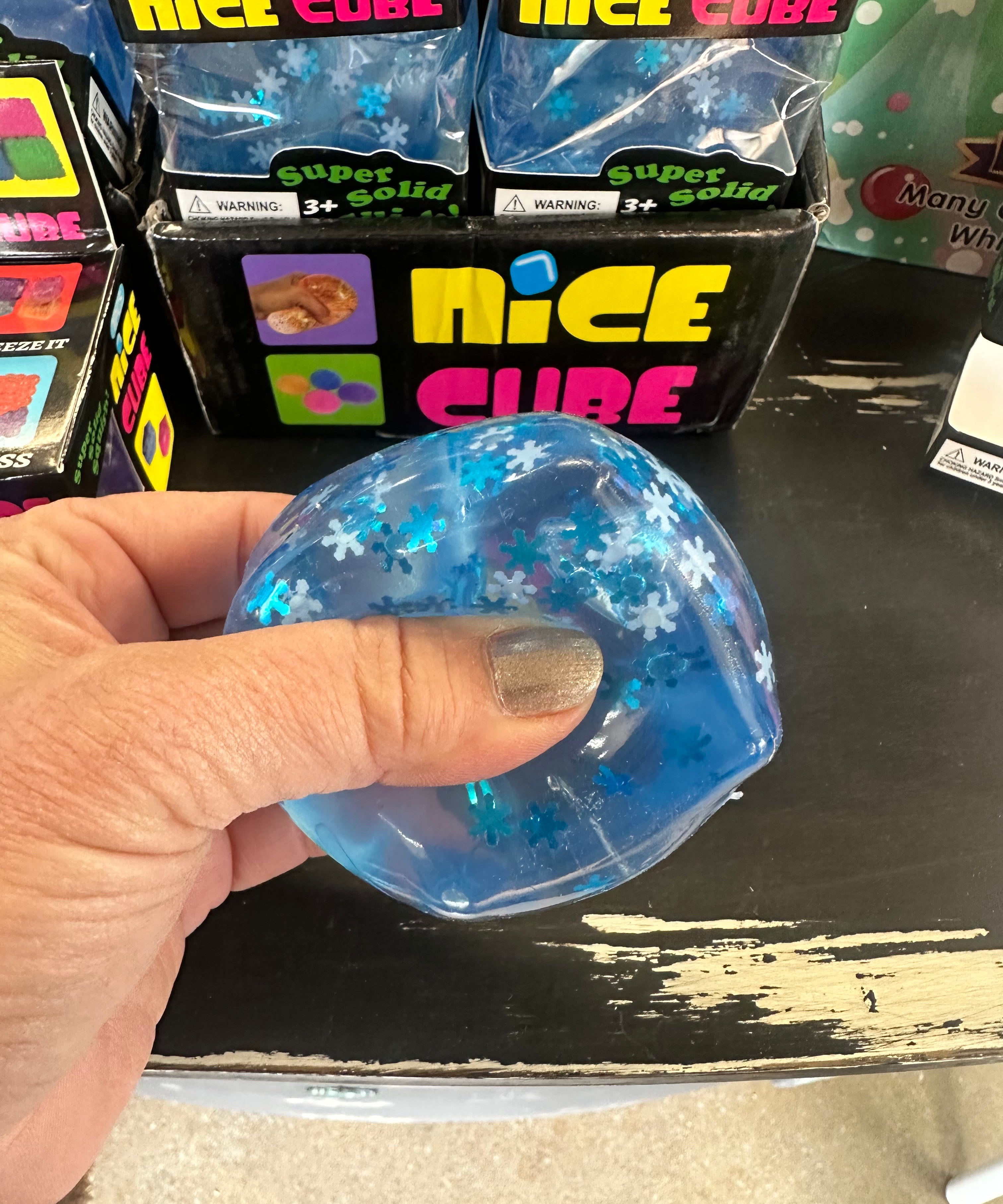 Blue glittery cube held by a hand with packaging labeled 'Nice Cube' in the background.