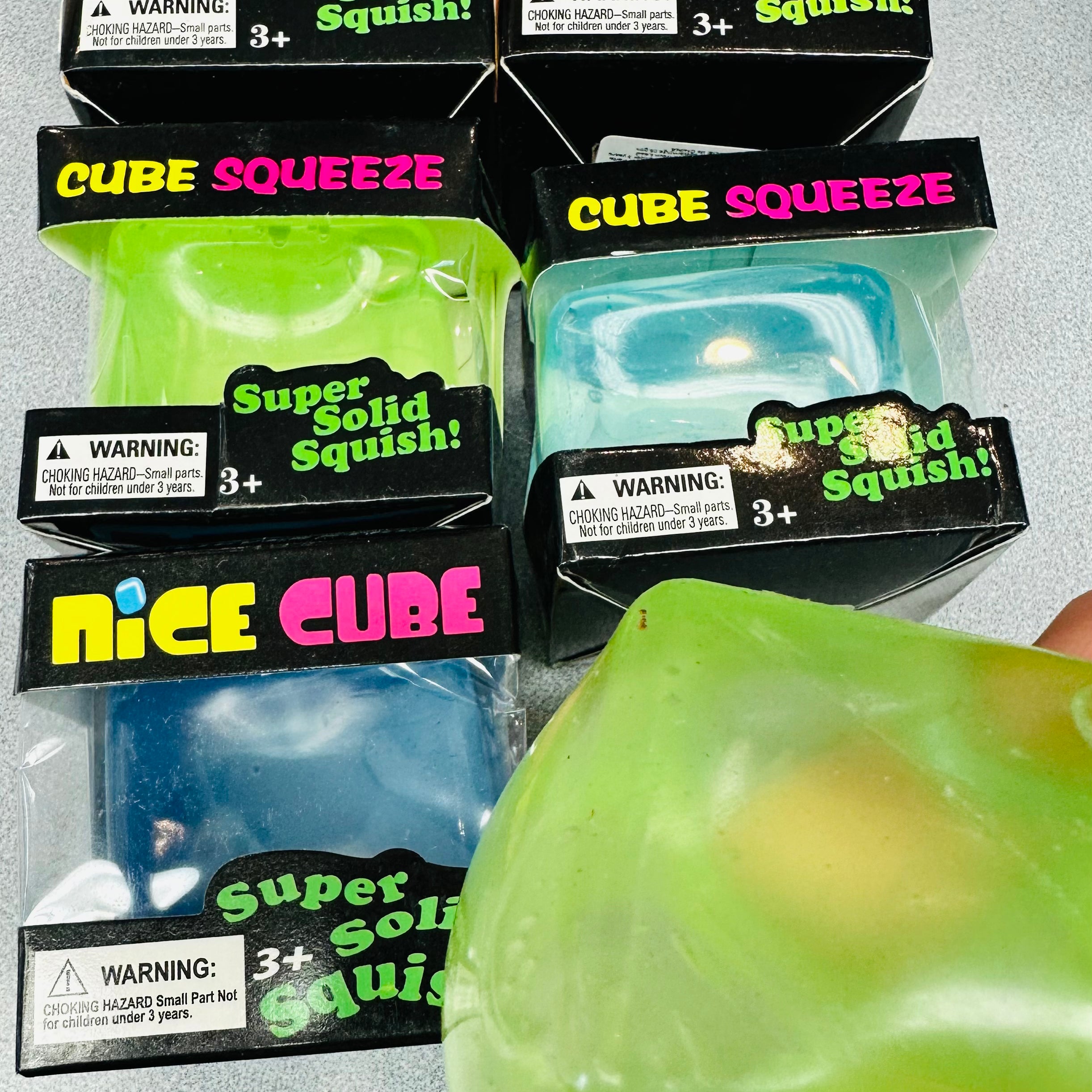 Packaged Cube Squeeze toys with a hand holding a green toy.