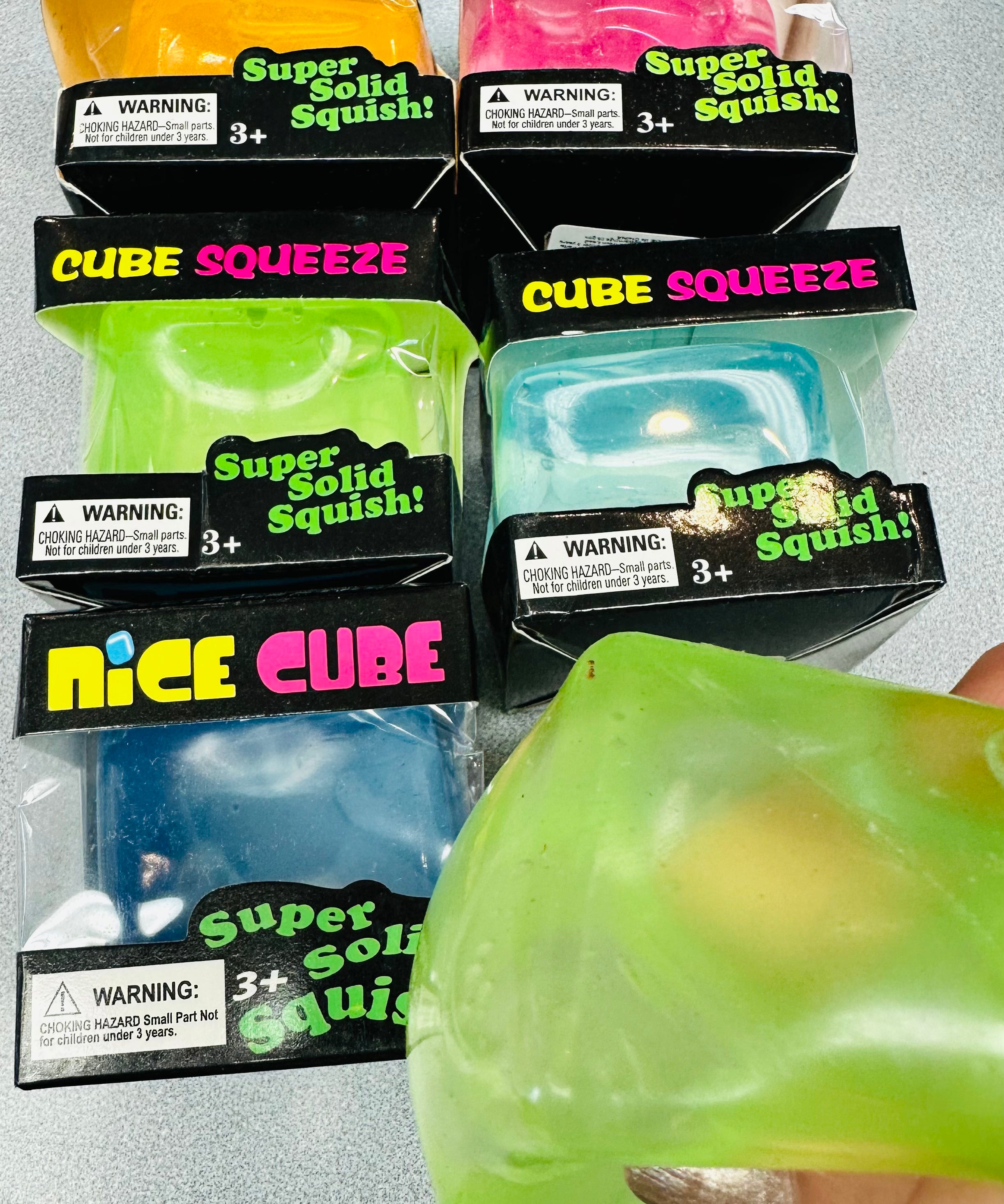 Packaged Cube Squeeze toys with a hand holding a green toy.