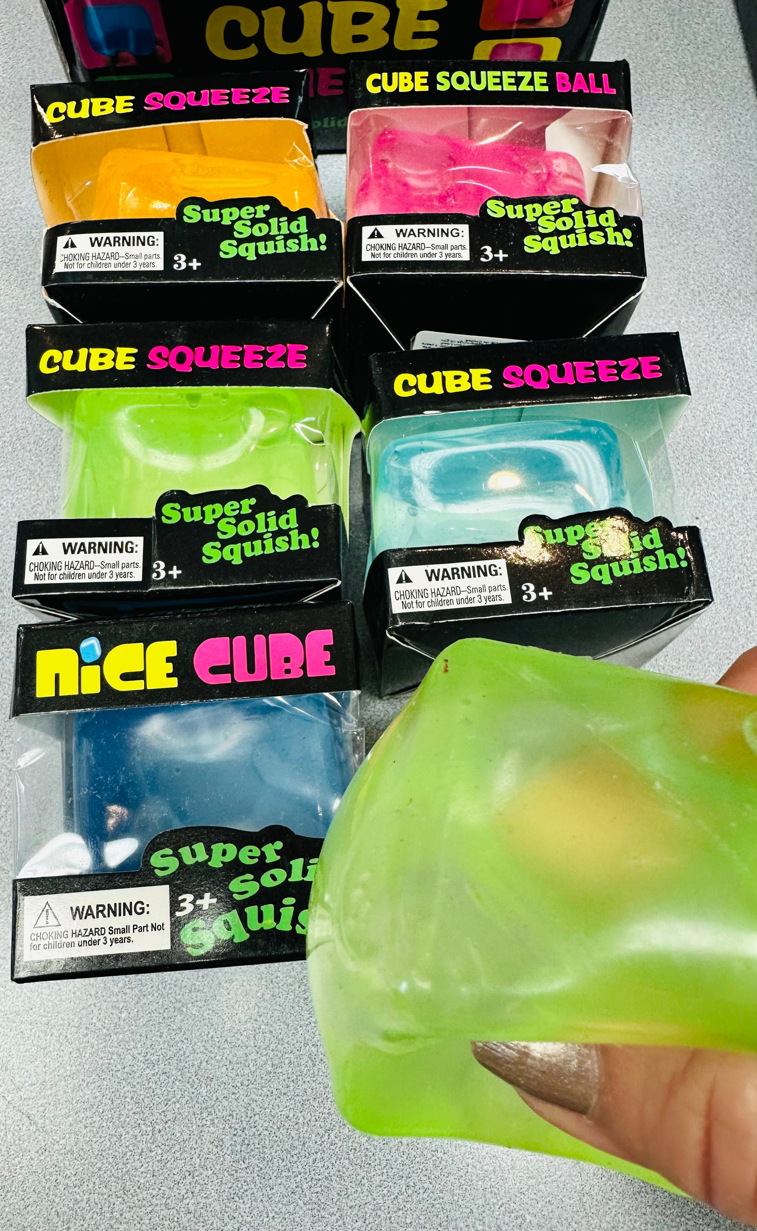 Packaged Cube Squeeze toys with a hand holding a green toy.