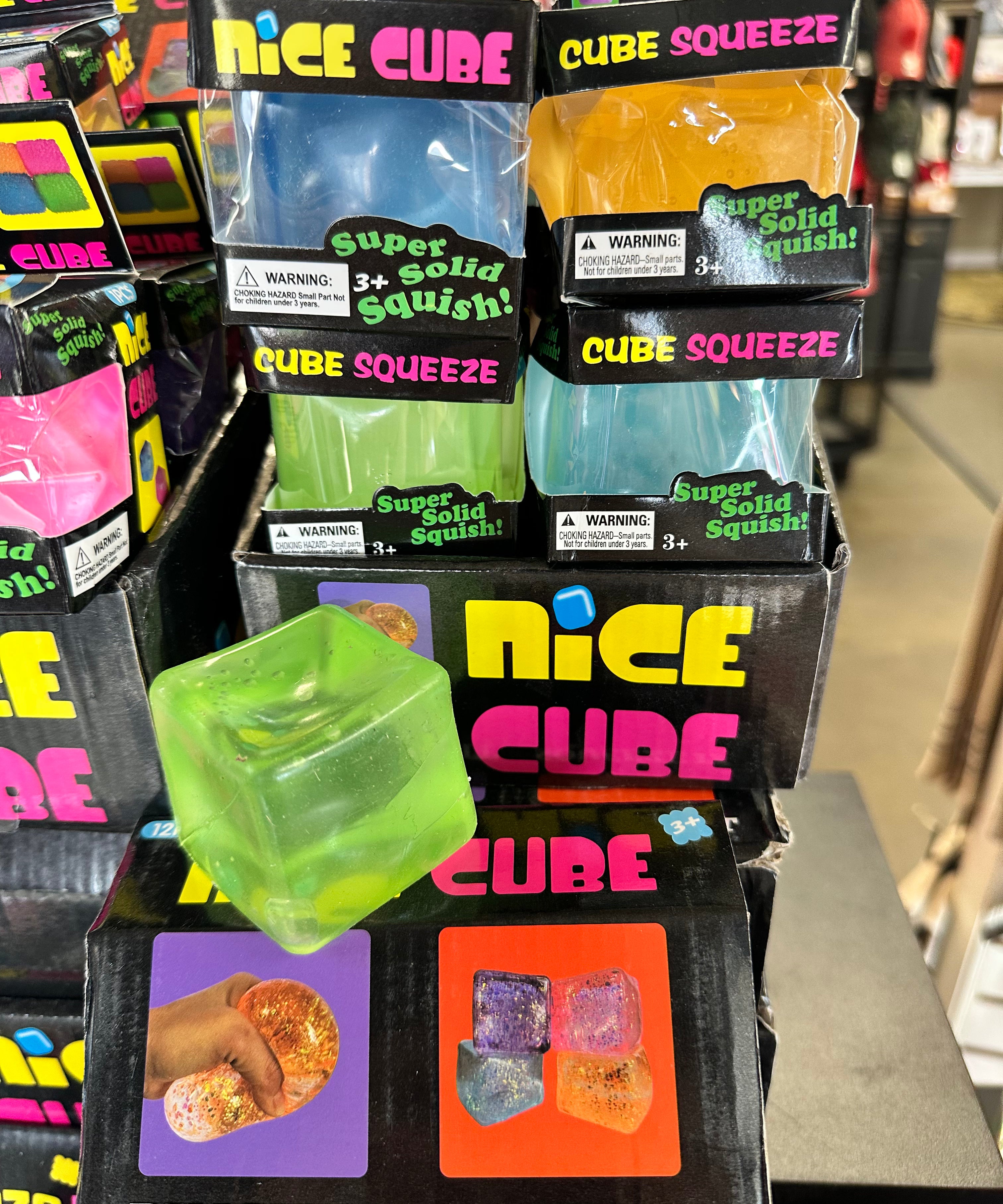 Stack of 'Nice Cube' packaging with colorful cubes on a store shelf.