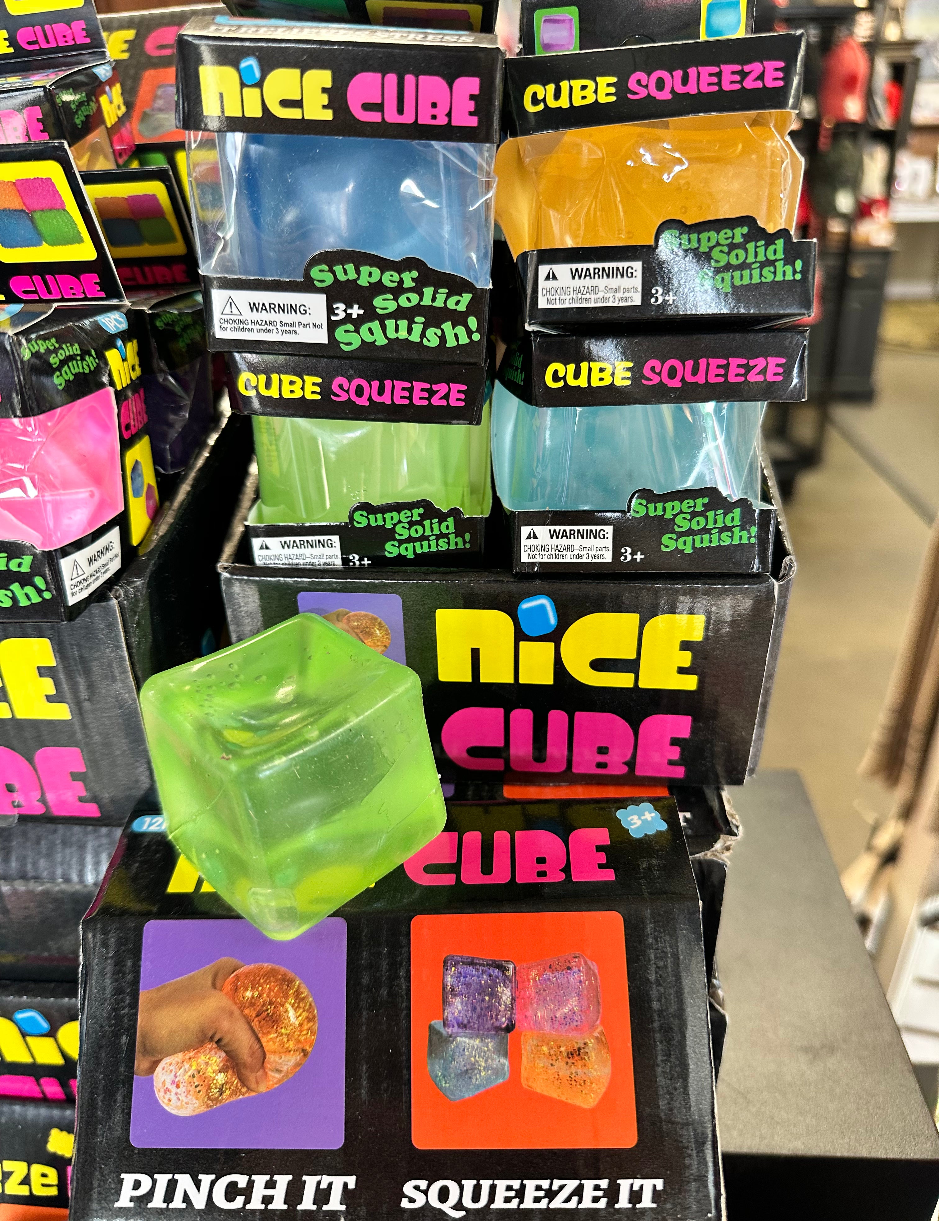 Stack of 'Nice Cube' packaging with colorful cubes on a store shelf.