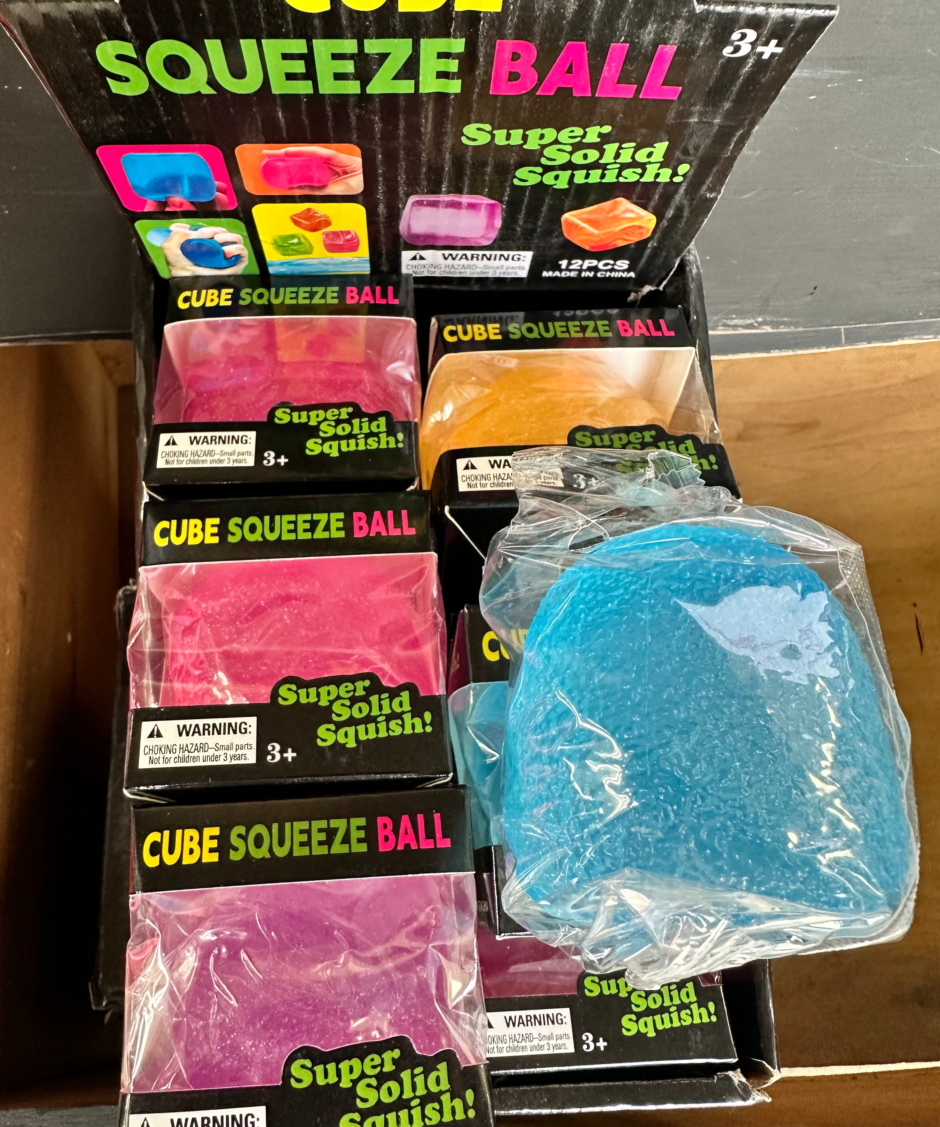Packaging of Cube Squeeze Balls with a blue ball outside the packaging.
