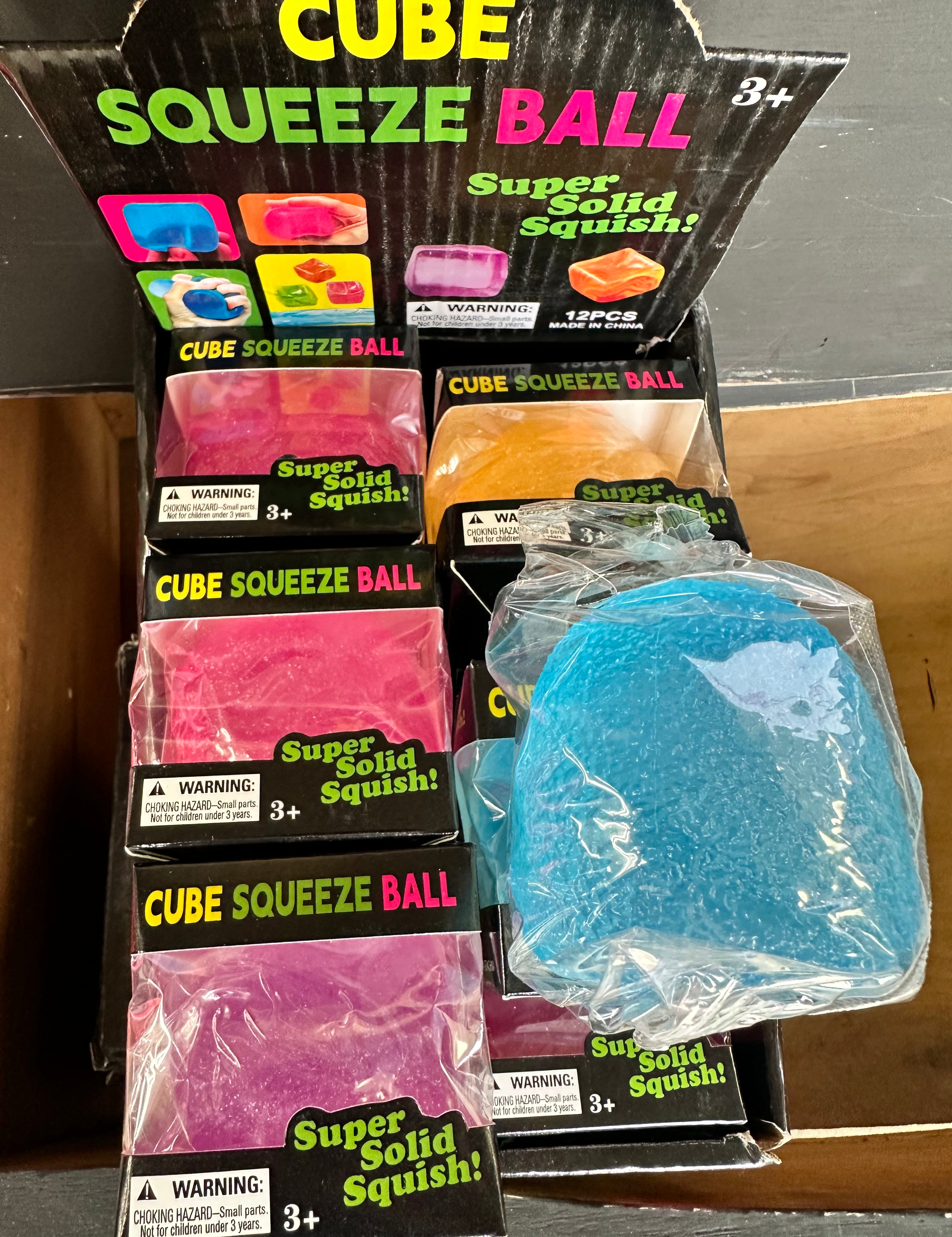 Packaging of Cube Squeeze Balls with a blue ball outside the packaging.