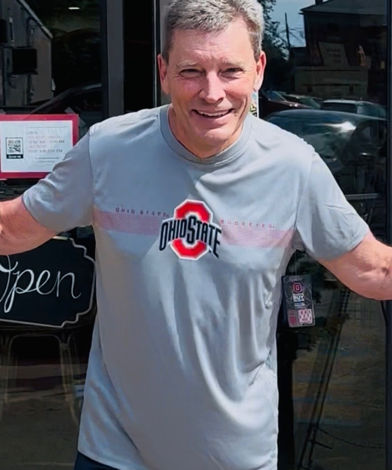 Man wearing a gray t-shirt with a logo, standing outside a building.