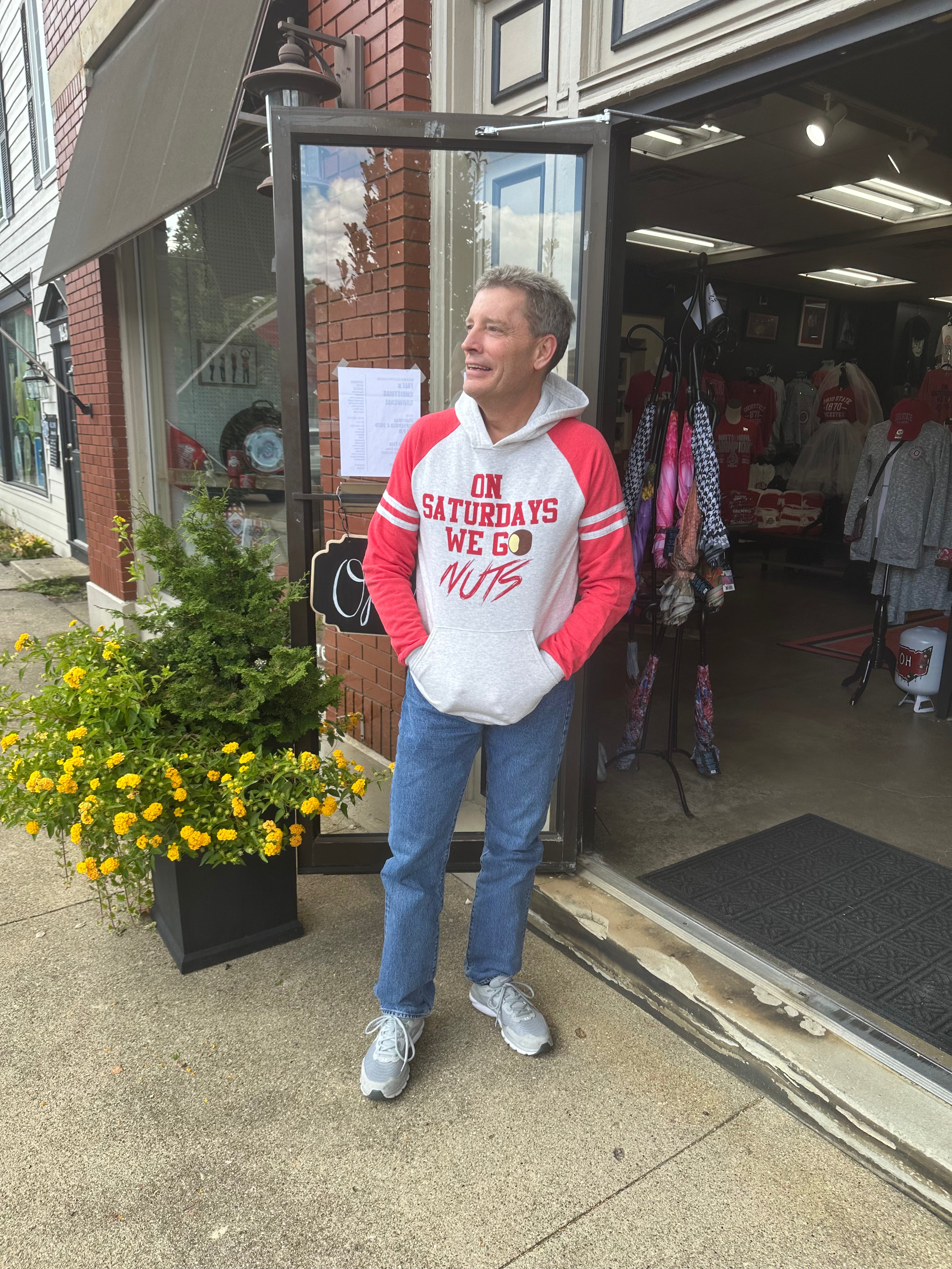 Man wearing a red and white hoodie standing outside a store with sweatshirt On Saturdays We Go Nuts.
