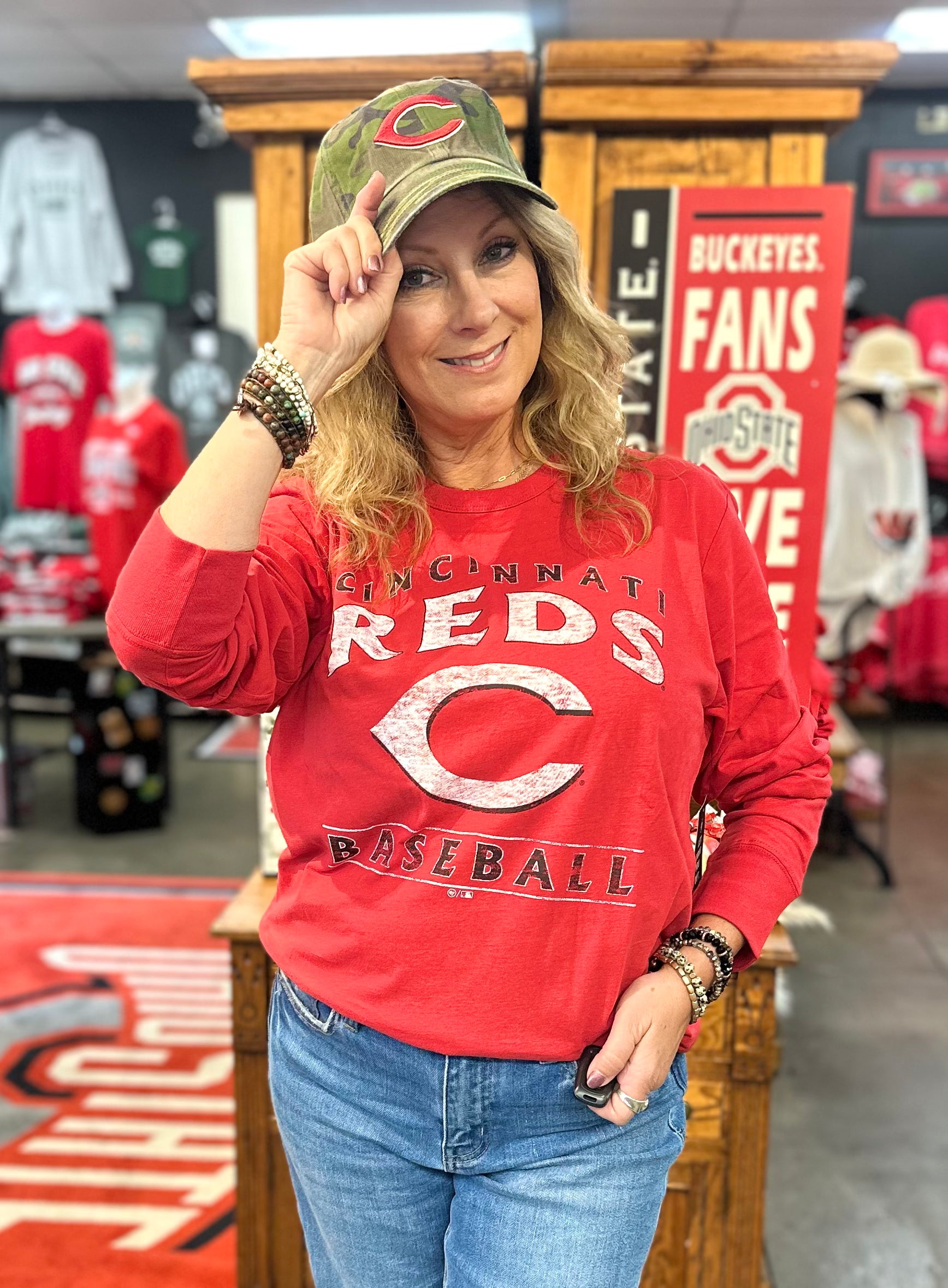 Woman wearing a red 'Cincinnati Reds' shirt and green cap in a sports store.