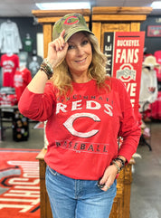 Woman wearing a red 'Cincinnati Reds' shirt and green cap in a sports store.