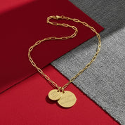 Gold chain necklace with two round pendants on a red and gray background