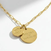 A gold paperclip chain necklace with two interlocking round gold pendants, one engraved with a geometric logo and the other with the engraved text 'LOYALTY FRIENDSHIP'.