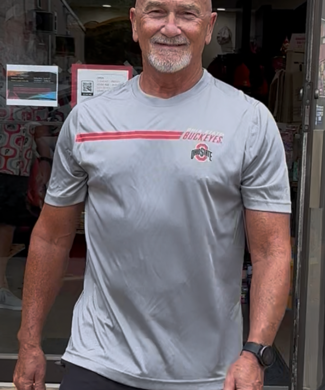Man wearing a gray t-shirt with a logo and text, standing indoors.