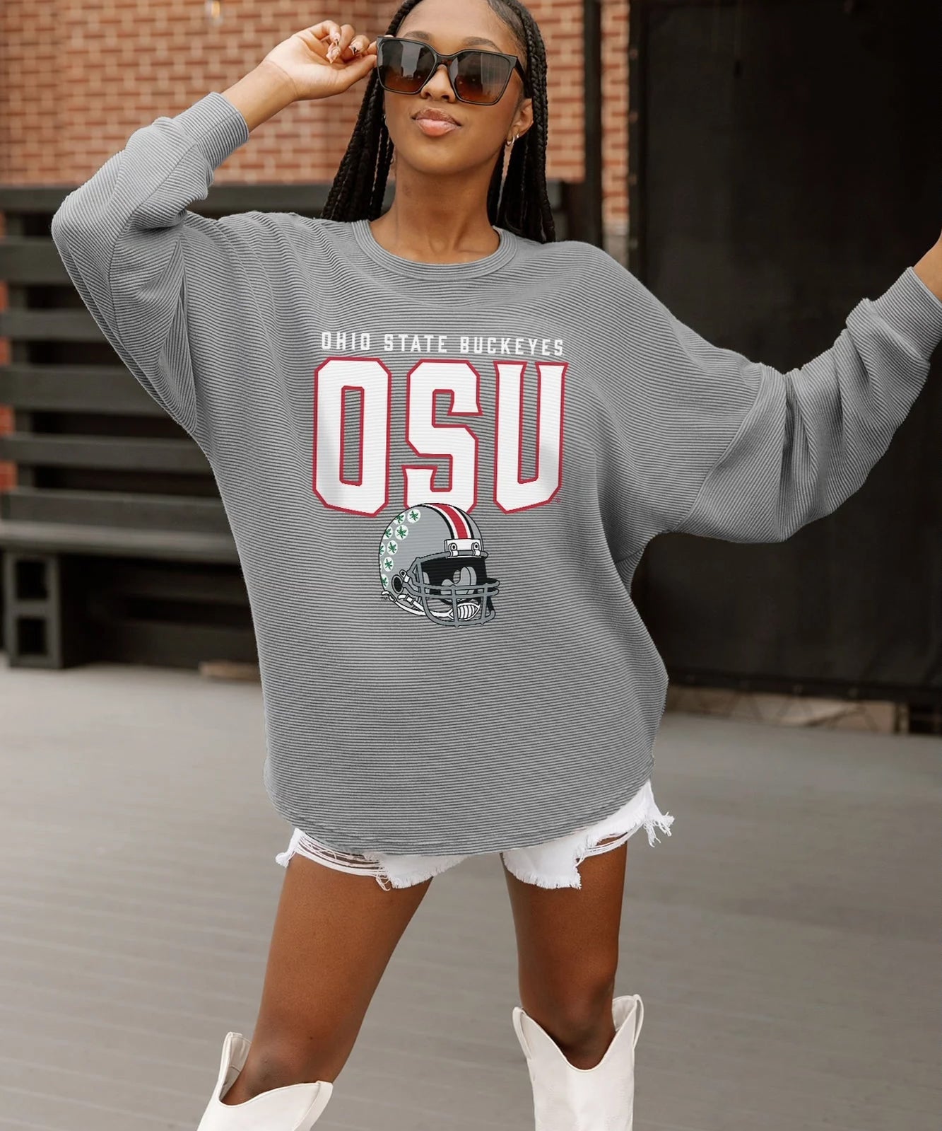 Woman wearing a gray sweatshirt with 'OSU' and a football helmet graphic, standing in front of a brick wall.