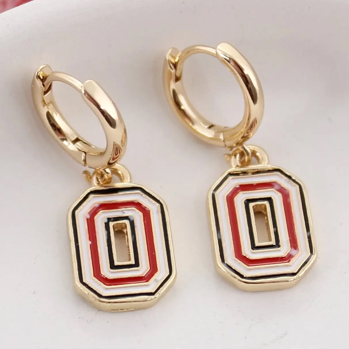 Gold hoop earrings with red, black, and white geometric drop charms on a light background