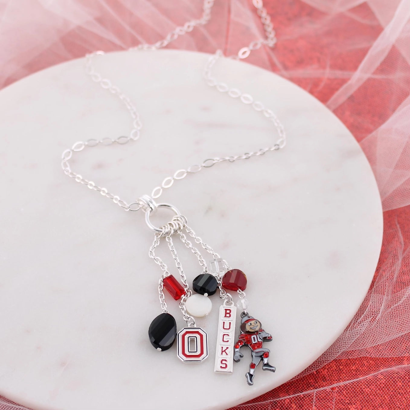 Necklace with sports-themed charms on a white dish with a red and white background