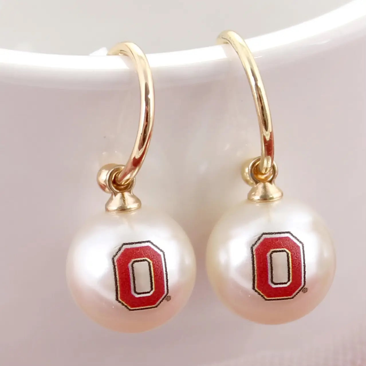 Pearl earrings with gold hooks and red 'O' logos on a white background